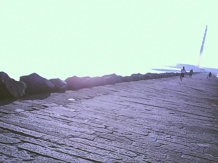 A hazy stone pier leading towards a distant lighthouse